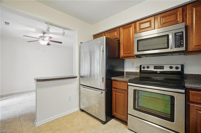 8530 Tidewater Dr Unit 111, Norfolk, VA 23503 - kitchen with stainless steel appliances, dark countertops, a ceiling fan, rail lighting, and brown cabinets
