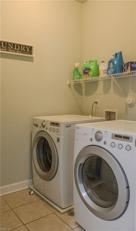 clothes washing area featuring washer and clothes dryer, light tile patterned floors, and baseboards