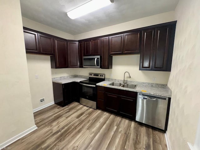kitchen featuring appliances with stainless steel finishes, a sink, light wood-type flooring, baseboards, and dark brown cabinetry