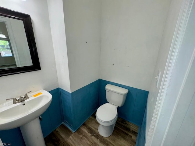 bathroom featuring wainscoting, wood finished floors, toilet, and a sink