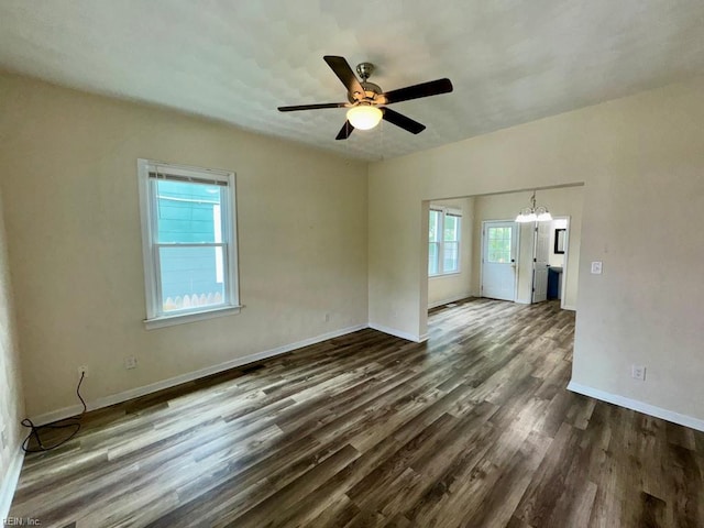 spare room featuring dark wood-style floors, baseboards, ceiling fan, and a chandelier
