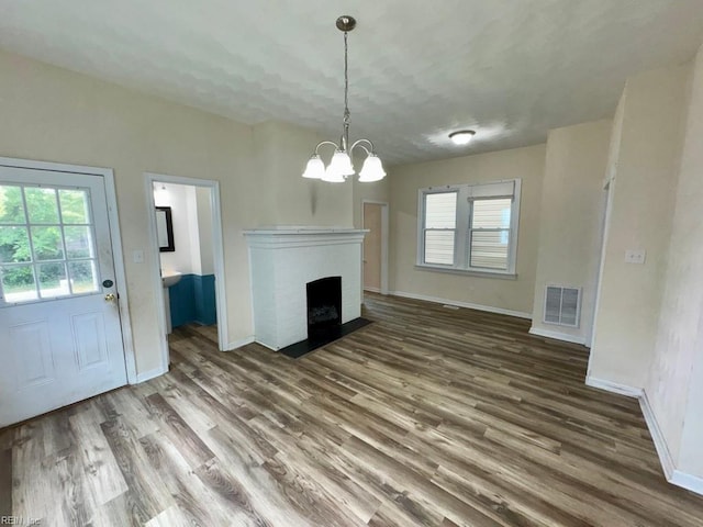 unfurnished living room with wood finished floors, baseboards, a chandelier, and a fireplace