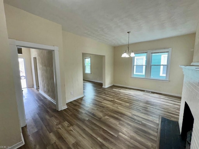 unfurnished living room featuring a fireplace, a chandelier, dark wood finished floors, and baseboards