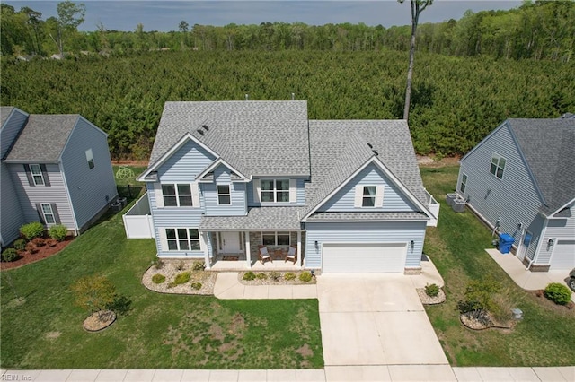 traditional home with a wooded view, a porch, a garage, a shingled roof, and concrete driveway