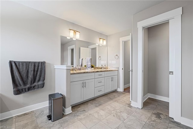 full bath featuring baseboards, double vanity, and marble look tile flooring