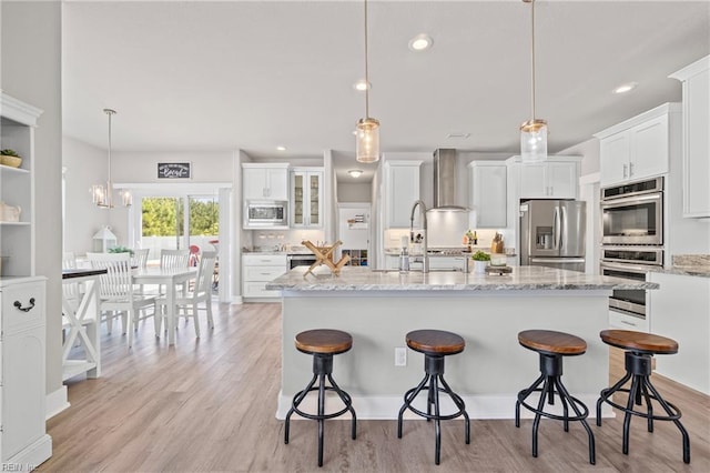 kitchen with appliances with stainless steel finishes, wall chimney exhaust hood, light wood-style flooring, white cabinetry, and recessed lighting