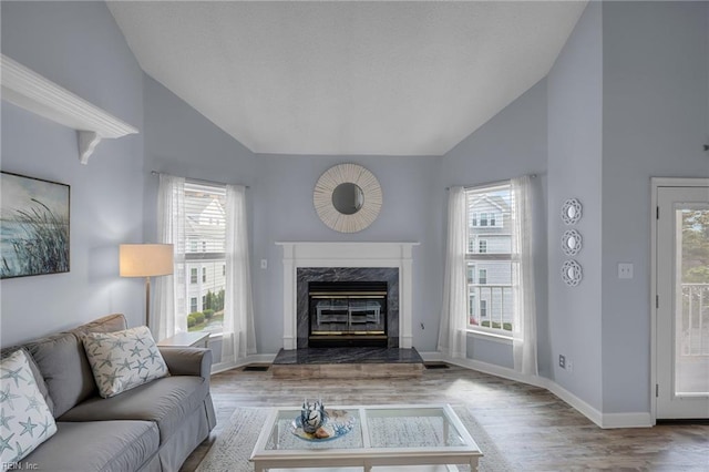 living area featuring a high end fireplace, wood finished floors, healthy amount of natural light, baseboards, and high vaulted ceiling