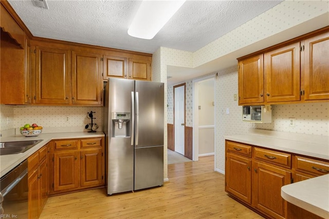 12 Critzos Ct, Hampton, VA 23669 - kitchen with stainless steel appliances, wallpapered walls, light wood finished floors, brown cabinetry, and a textured ceiling