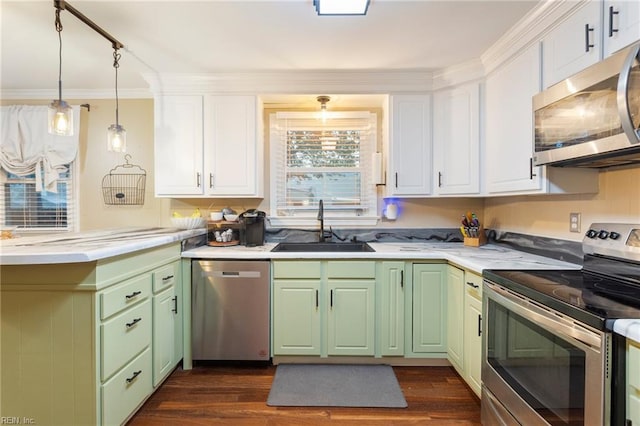 kitchen with appliances with stainless steel finishes, a sink, green cabinetry, a peninsula, and crown molding