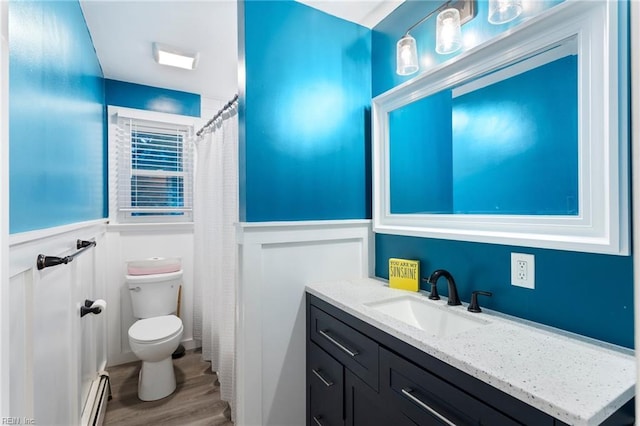 bathroom with a baseboard heating unit, wood finished floors, toilet, a wainscoted wall, and vanity