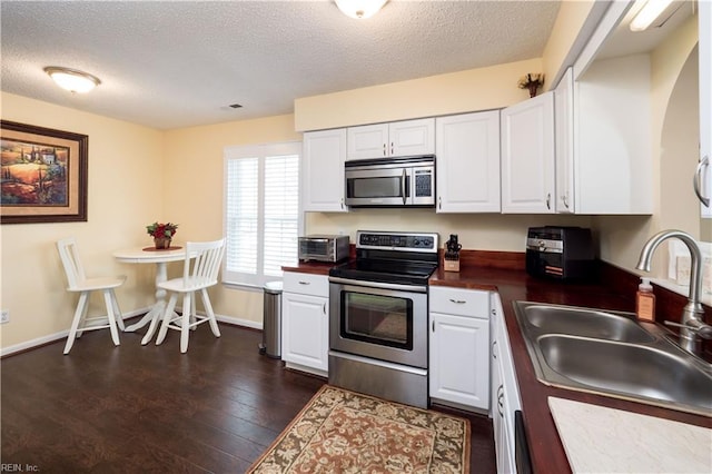 kitchen featuring stainless steel appliances, a sink, a textured ceiling, white cabinets, and dark countertops