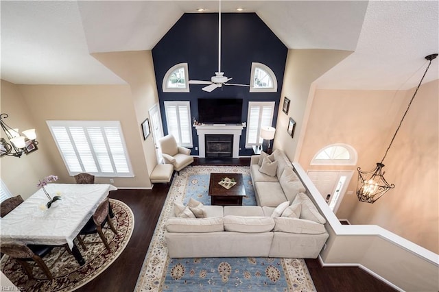 living area with a chandelier, a ceiling fan, dark wood finished floors, and a high ceiling