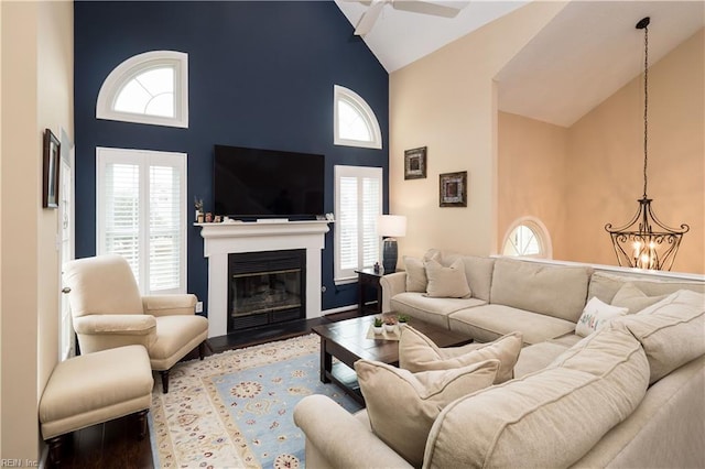 living room featuring high vaulted ceiling, a chandelier, wood finished floors, ceiling fan, and a fireplace with flush hearth