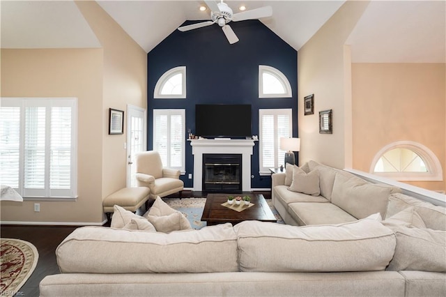 living room featuring a ceiling fan, high vaulted ceiling, dark wood-type flooring, a glass covered fireplace, and plenty of natural light
