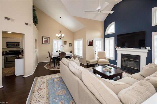 living room with high vaulted ceiling, dark wood-type flooring, a chandelier, a glass covered fireplace, and ceiling fan