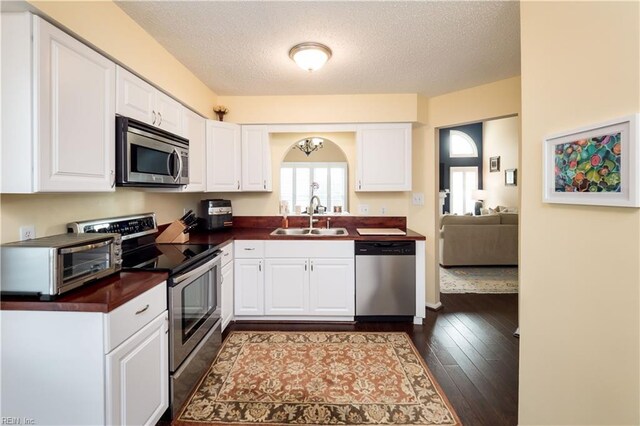 kitchen featuring appliances with stainless steel finishes, a sink, white cabinets, a textured ceiling, and dark wood-style flooring