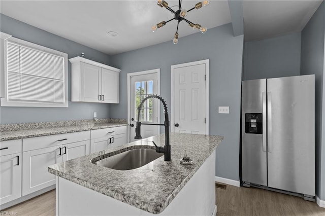 kitchen featuring stainless steel fridge, a sink, light wood-style flooring, white cabinetry, and light stone counters