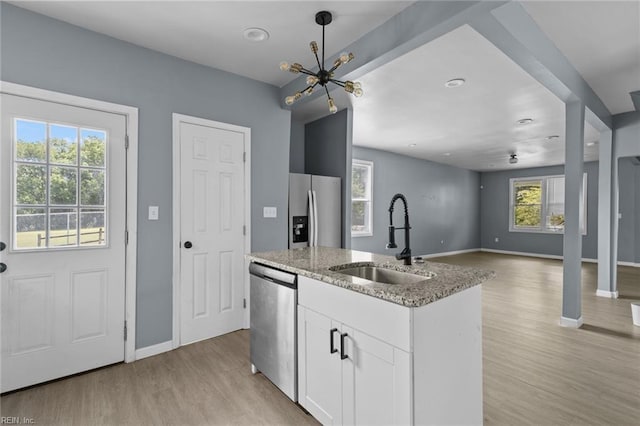 kitchen featuring a sink, stainless steel appliances, baseboards, light wood-style floors, and light stone counters