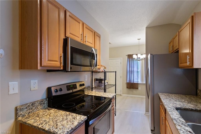 117 Bute St, Suffolk, VA 23434 - kitchen featuring appliances with stainless steel finishes, a chandelier, brown cabinetry, light stone counters, and light wood-type flooring