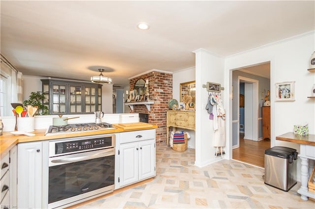kitchen featuring stainless steel appliances, butcher block counters, white cabinetry, crown molding, and glass insert cabinets