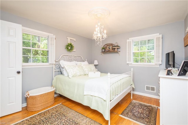 bedroom featuring multiple windows, wood finished floors, baseboards, and a chandelier