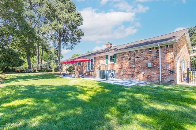 rear view of property featuring a patio area, central AC unit, a chimney, and brick siding