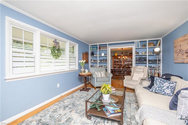 living area with wood finished floors, a chandelier, crown molding, baseboards, and built in features