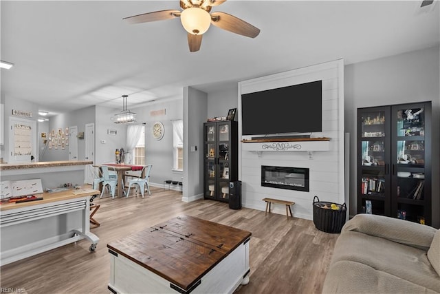 living room with wood finished floors, a fireplace, a ceiling fan, and baseboards