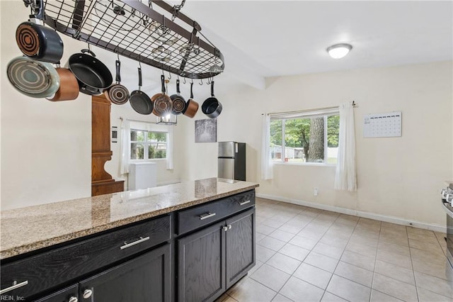 kitchen with healthy amount of natural light, freestanding refrigerator, dark cabinetry, and light tile patterned floors