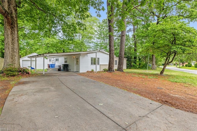 view of front facade with driveway, a carport, and view of wooded area