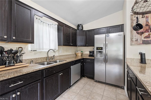 kitchen with appliances with stainless steel finishes, a sink, vaulted ceiling, light tile patterned floors, and light stone counters