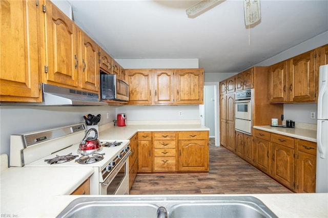 13542 Brink Rd, Emporia, VA 23847 - kitchen with white appliances, under cabinet range hood, dark wood-style floors, light countertops, and brown cabinetry