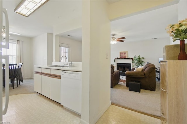 kitchen with white dishwasher, a sink, light floors, and plenty of natural light