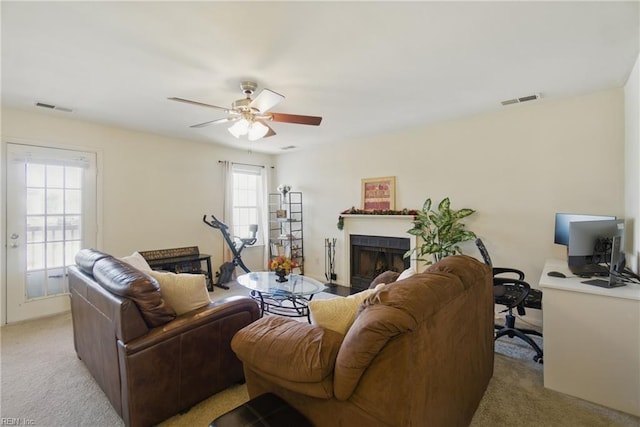living room with light colored carpet, ceiling fan, a fireplace, and a desk