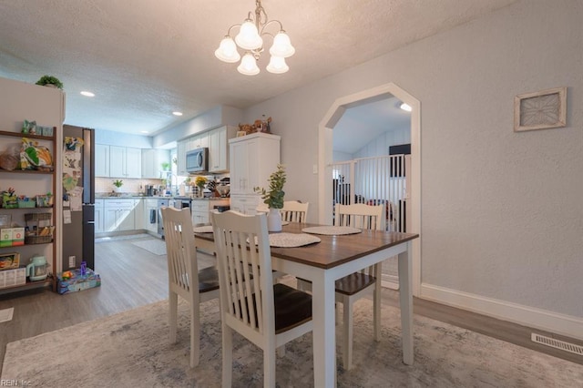 310 Manteo Ave, Hampton, VA 23661 - dining area featuring light wood-type flooring, a textured ceiling, a chandelier, arched walkways, and a textured wall