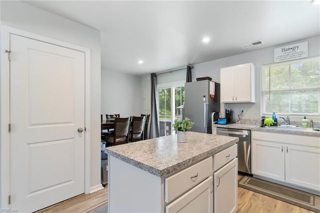 kitchen with stainless steel appliances, light wood finished floors, a kitchen island, white cabinets, and light countertops