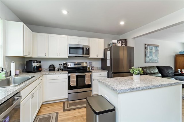 kitchen with stainless steel appliances, light wood-style floors, a center island, a sink, and white cabinets