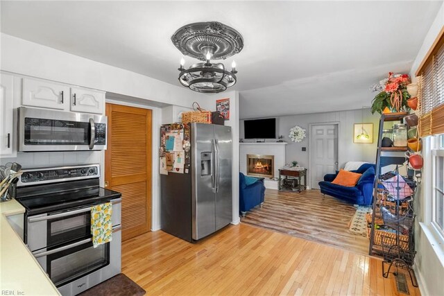 4769 Marlborough Dr, Virginia Beach, VA 23464 - kitchen featuring appliances with stainless steel finishes, white cabinetry, light wood-type flooring, a glass covered fireplace, and a chandelier