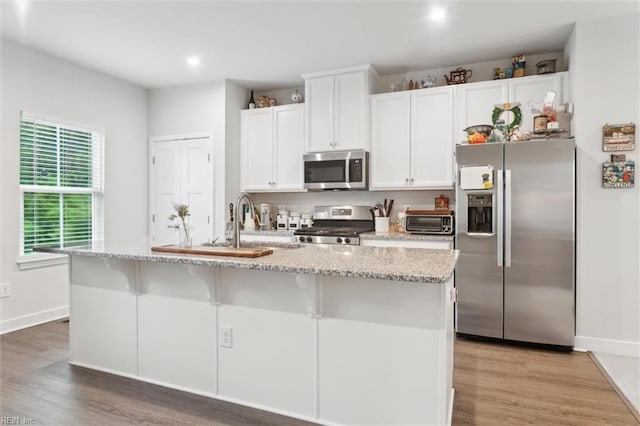 109 Big Woods Dr, Poquoson, VA 23662 - kitchen with stainless steel appliances, a kitchen island with sink, white cabinets, light wood-style flooring, and baseboards