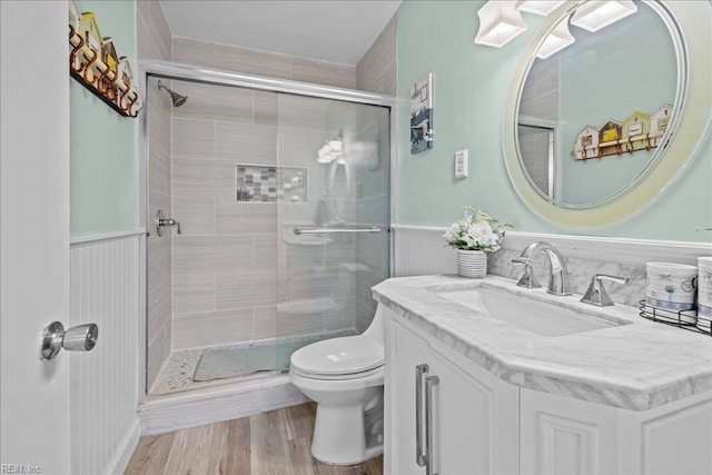 full bathroom with a stall shower, a wainscoted wall, toilet, vanity, and wood finished floors