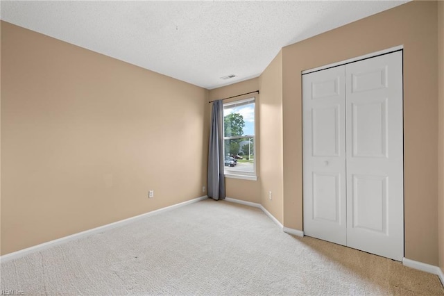 unfurnished bedroom with light carpet, baseboards, a textured ceiling, and a closet