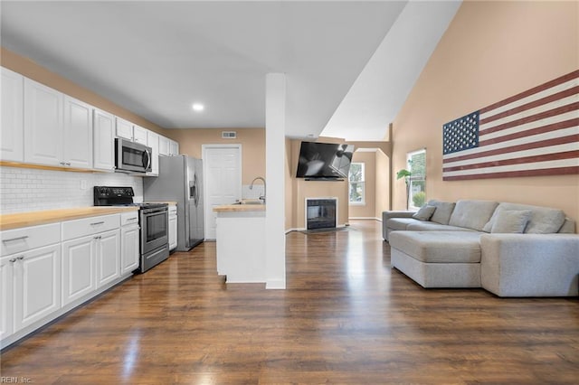 living room with dark wood-style flooring, a fireplace with flush hearth, recessed lighting, a towering ceiling, and baseboards