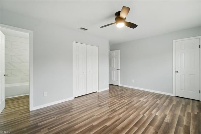 unfurnished bedroom featuring wood finished floors, a closet, baseboards, and ensuite bath