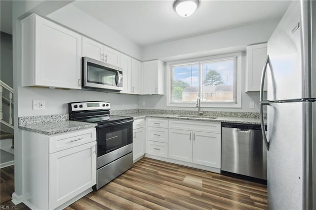 kitchen featuring stainless steel appliances, a sink, dark wood-style flooring, white cabinetry, and light stone countertops
