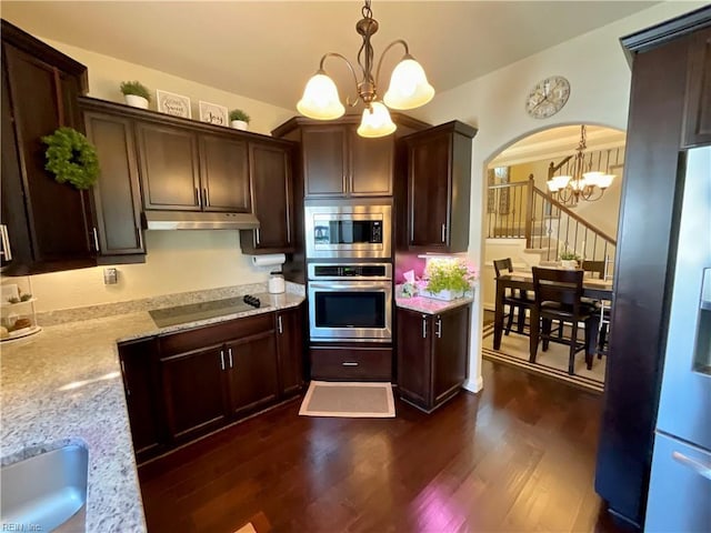 kitchen featuring appliances with stainless steel finishes, a chandelier, under cabinet range hood, arched walkways, and dark wood-style flooring