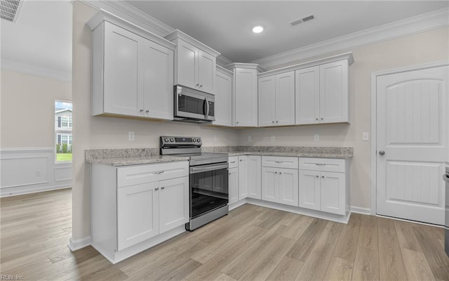 kitchen with stainless steel appliances, ornamental molding, light wood finished floors, light stone countertops, and white cabinets