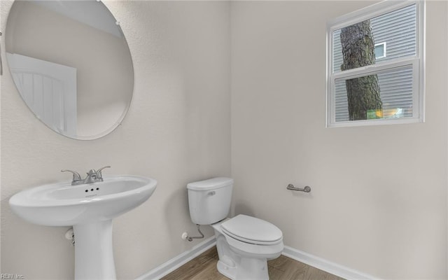 half bathroom with toilet, wood finished floors, and baseboards
