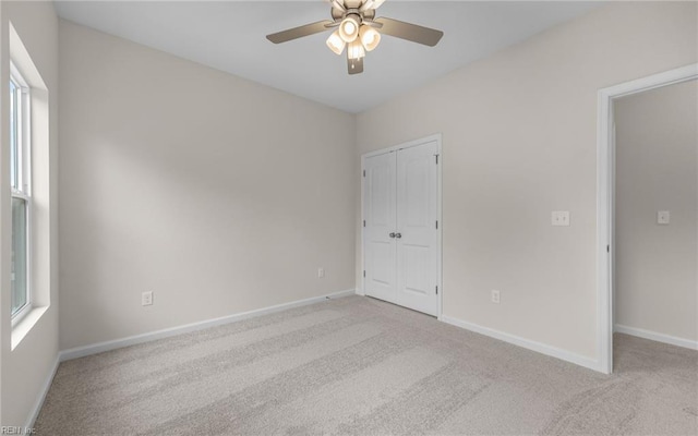 unfurnished bedroom with light colored carpet, a closet, baseboards, ceiling fan, and multiple windows