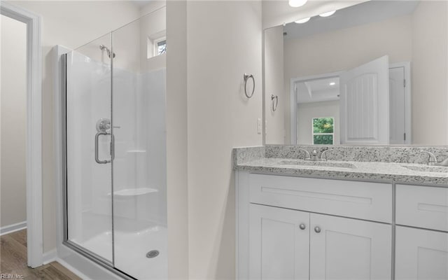 full bathroom featuring a stall shower, double vanity, and wood finished floors