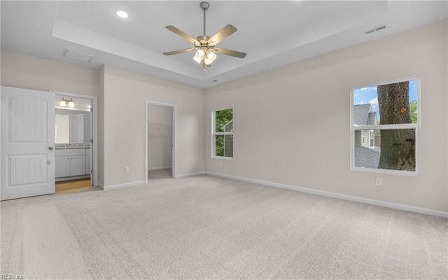 unfurnished bedroom featuring light carpet, a tray ceiling, a spacious closet, baseboards, and recessed lighting